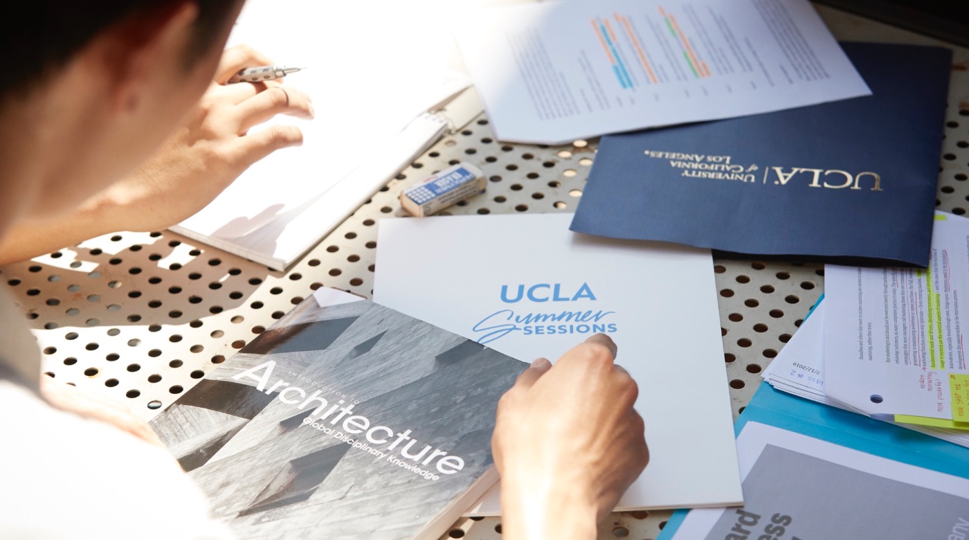 Student looking over a UCLA Summer Sessions folder and architecture textbook.