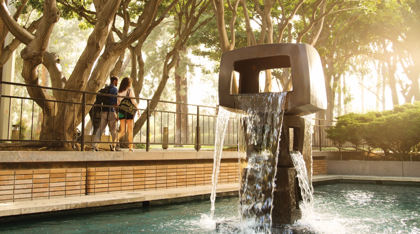View of cubed sculpture in a fountain at the Sculpture Garden as two students walk past.