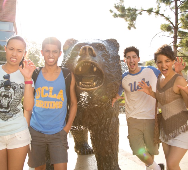 Four students posing in front of the Bruin bear. All four students are imitating the Bruin bear by posing with their mouths open and arms out.