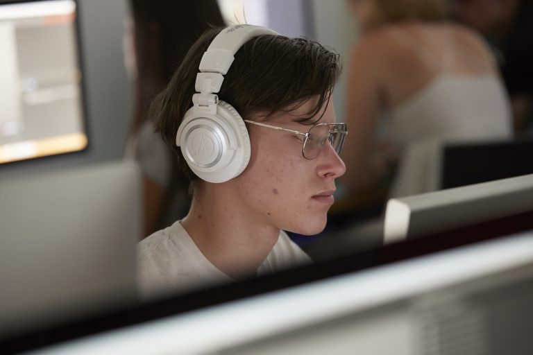 Closeup of a male student wearing white headphones looking at a computer.