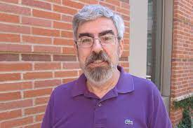 Portrait of David Smallberg. He is wearing a casual purple shirt and standing in front of a brick building.