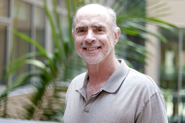Portrait of Richard Korf. He is wearing a casual grey shirt standing in front of a palm tree.