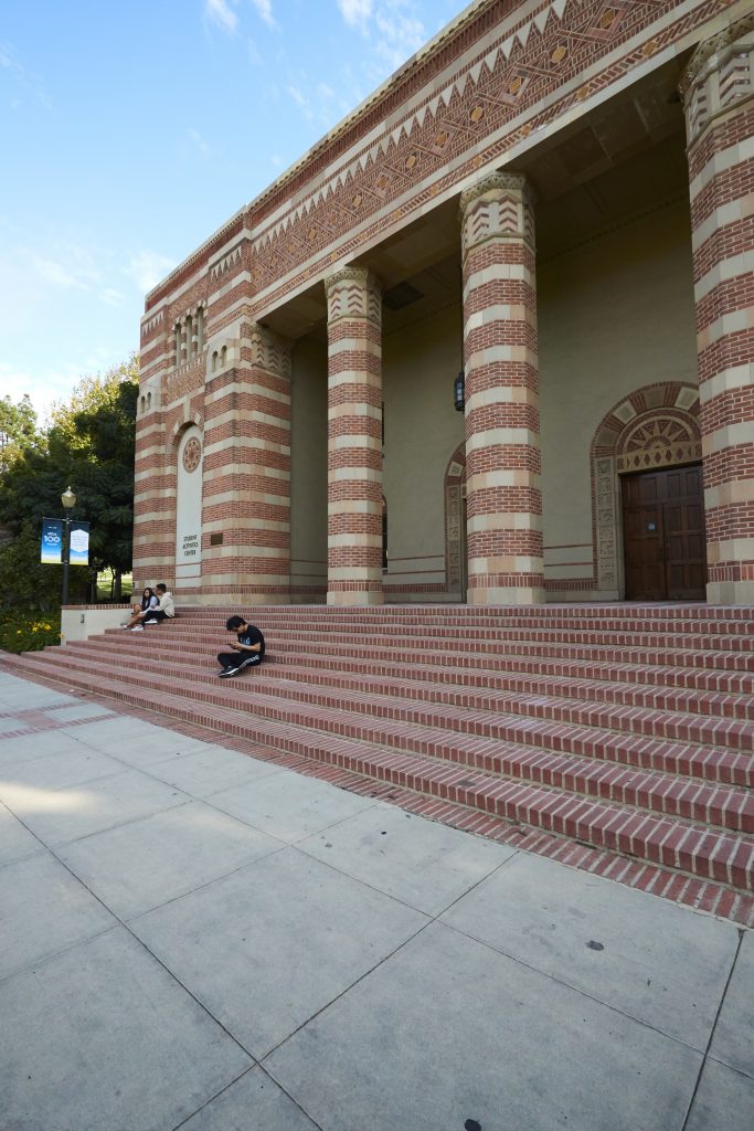 A few students sit on the steps of the Student Activities Center, which has a decorative red brick facade and columns.