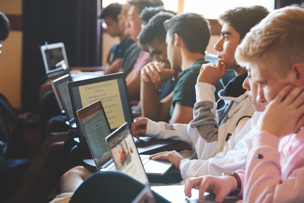 A row of students with laptops listening to a lecture in a lecture hall .