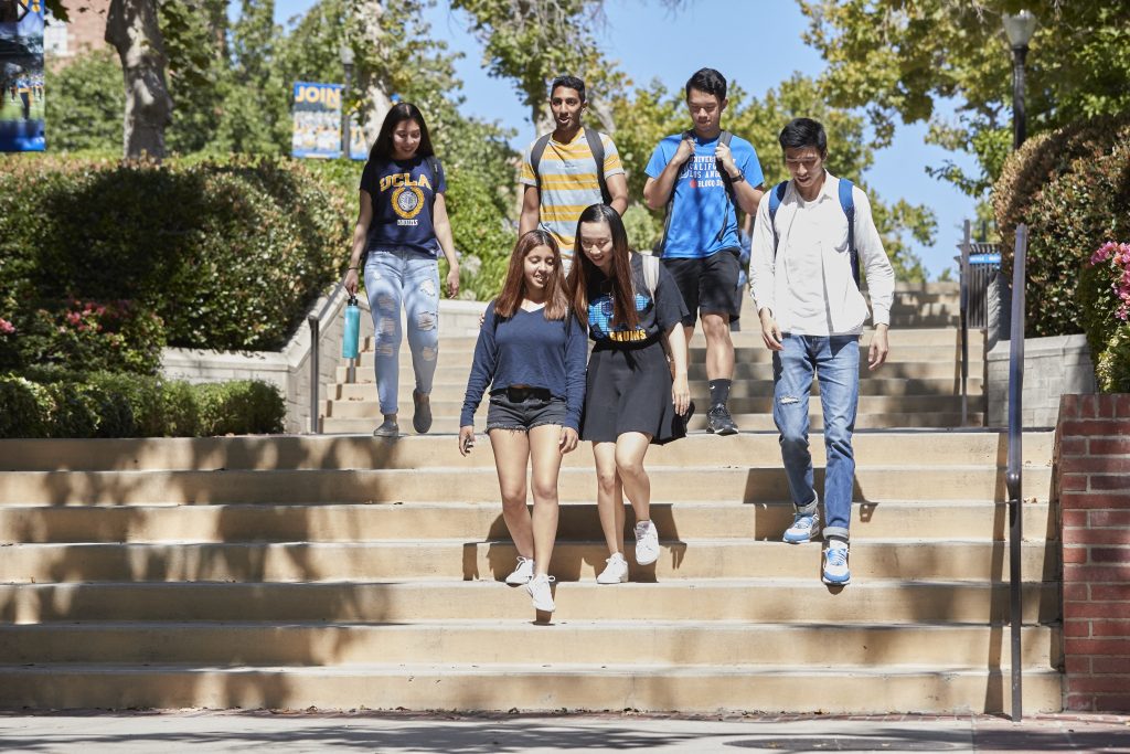 Six students talk to each other and walk down steps on the UCLA campus.
